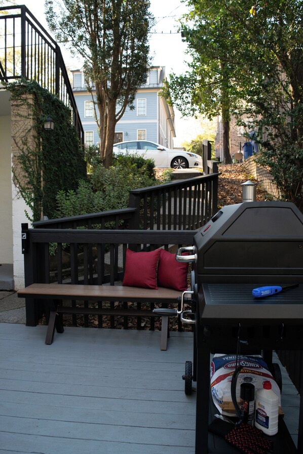 Une terrasse avec un barbecue, un banc en bois et un coussin rouge.