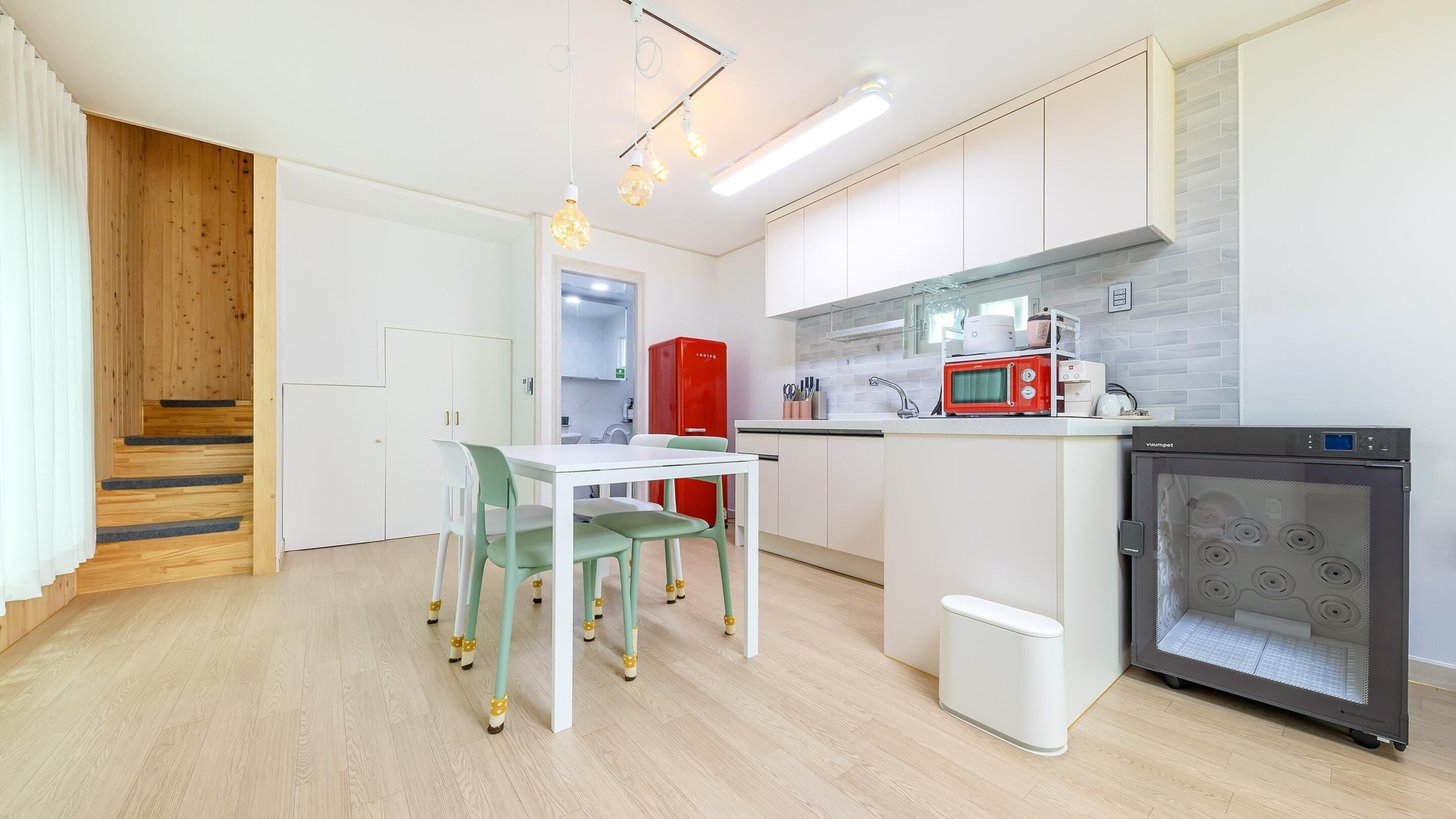 A modern kitchen with white cabinets, a red refrigerator, a microwave, and a built-in oven.
