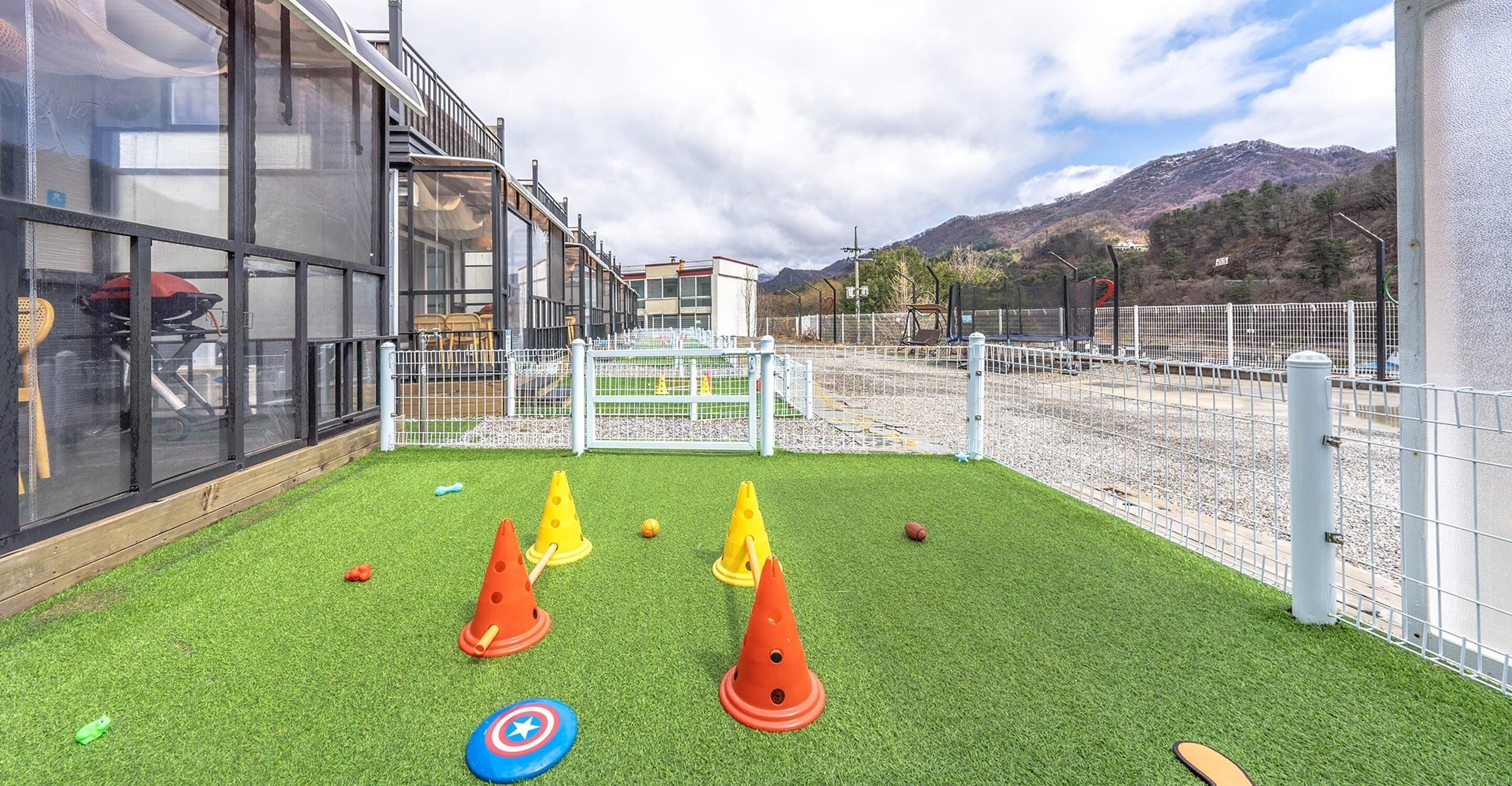 An outdoor play area with artificial grass, a white fence, and a mountain view in the background.