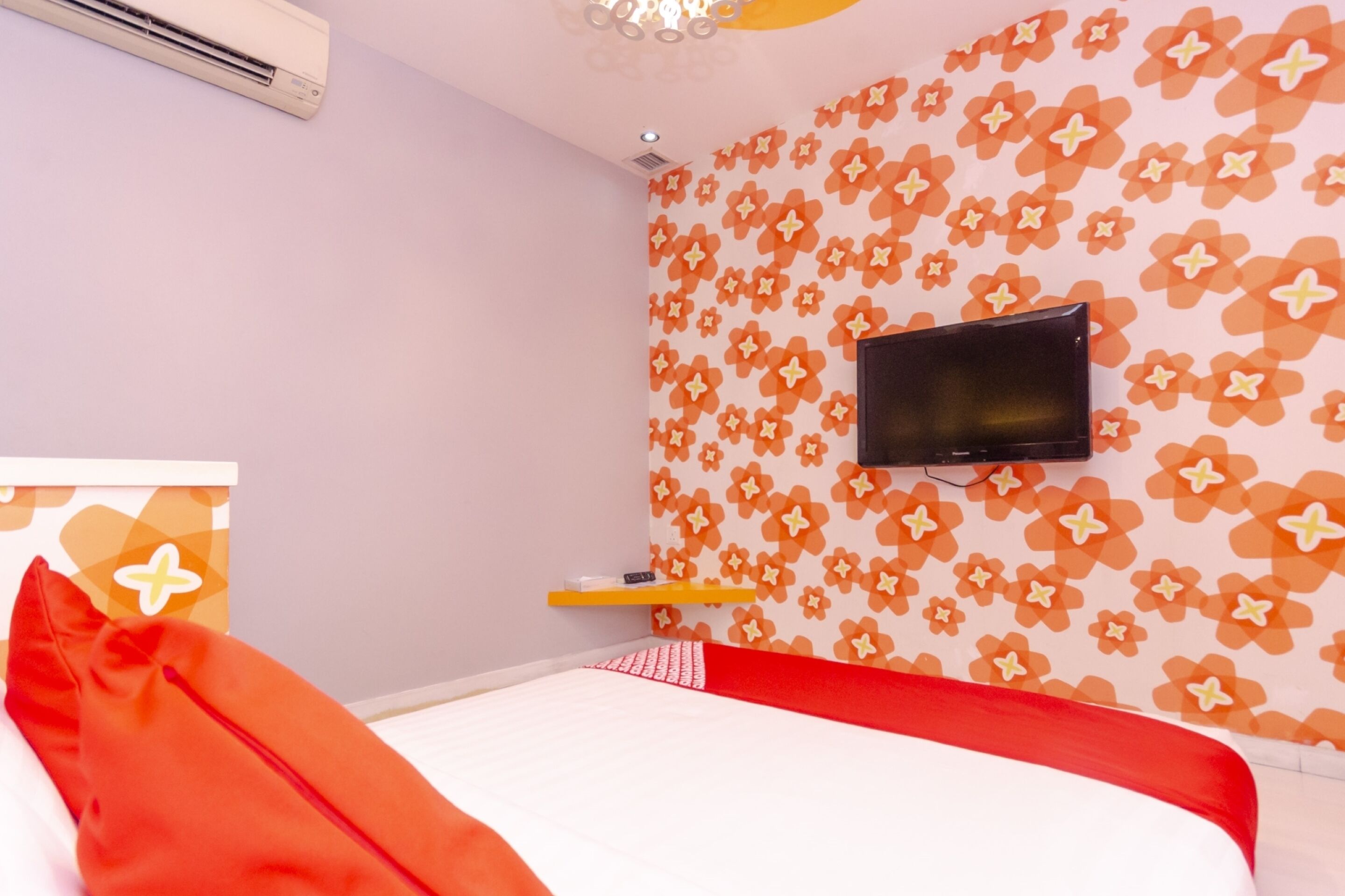 Une chambre à coucher avec un lit, un téléviseur fixé au mur et un mur orné d’un motif floral.
