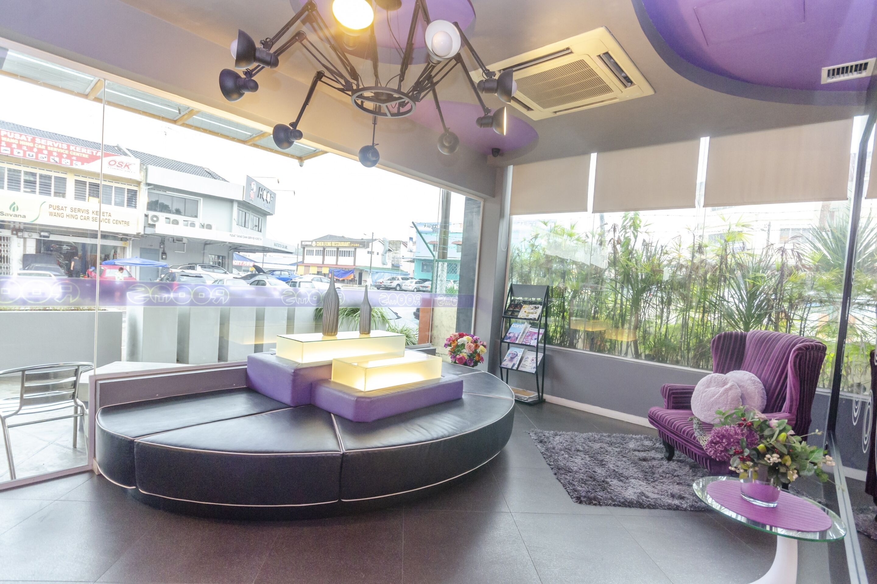 A modern reception area with a curved seating area, a glass display table with a vase of flowers, and a view of the street outside.