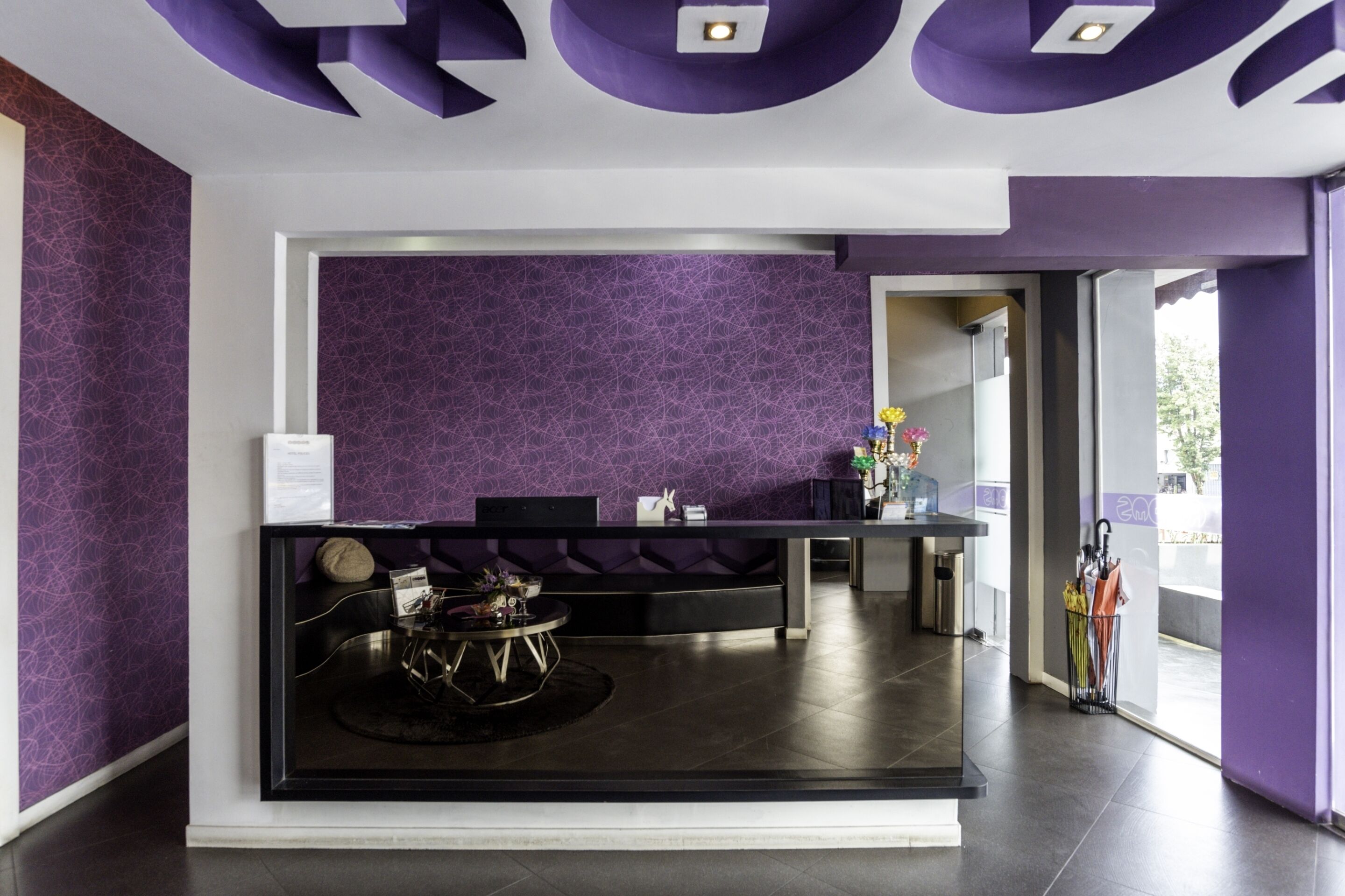 A reception area with a purple patterned wall, a reception desk, and a seating area with a round table.