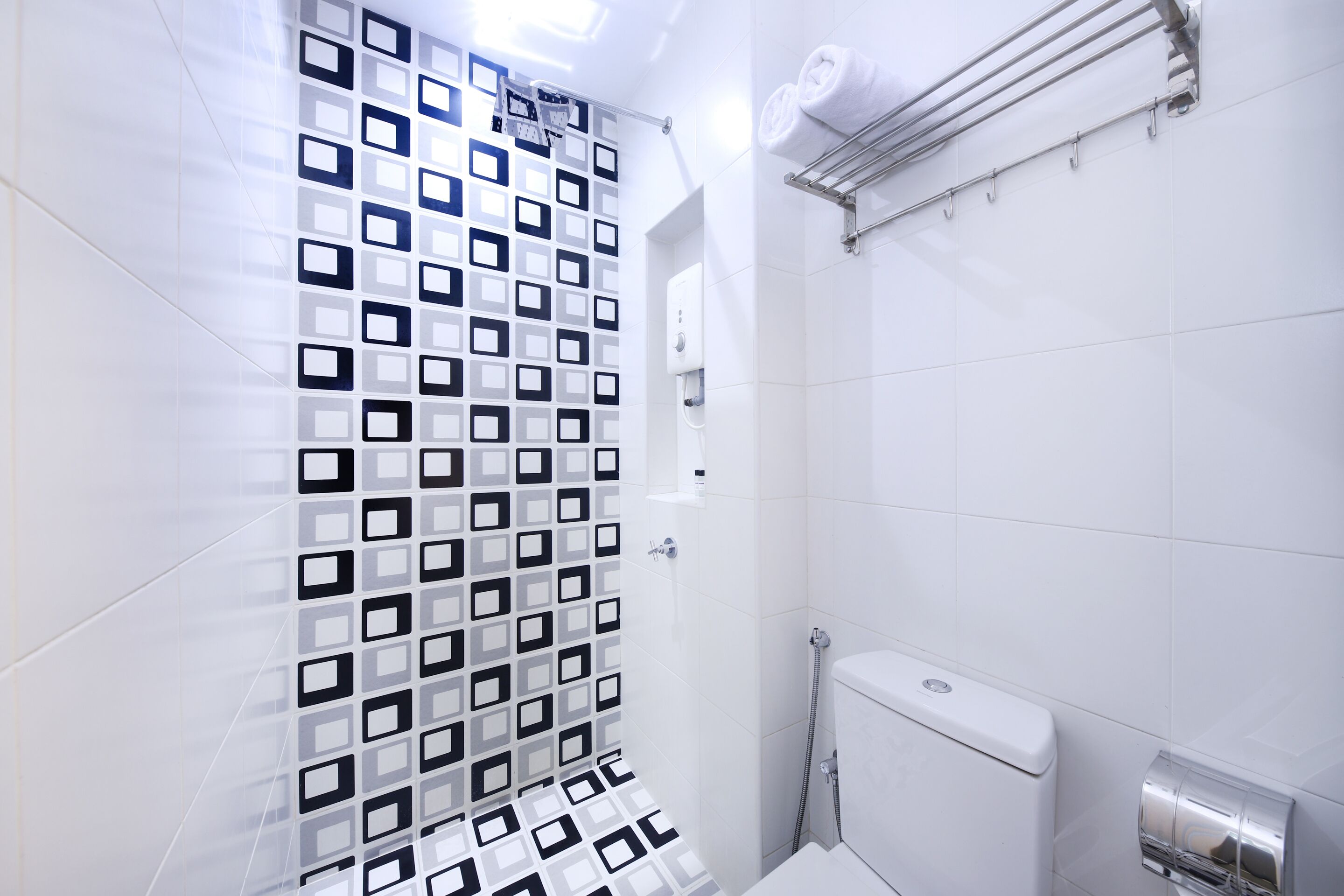 A modern bathroom with a geometric tile pattern, a toilet, and a towel rack.