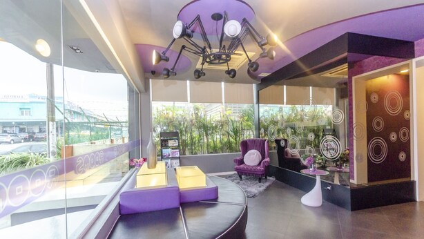 Een moderne hotelentree met een gebogen zithoek, een paarse fauteuil en een groot raam met uitzicht op groen en een brug.