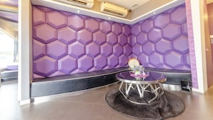Een moderne lobby met een paars, zeshoekig wandontwerp, een ronde tafel met een vaas en airconditioningunits aan het plafond.