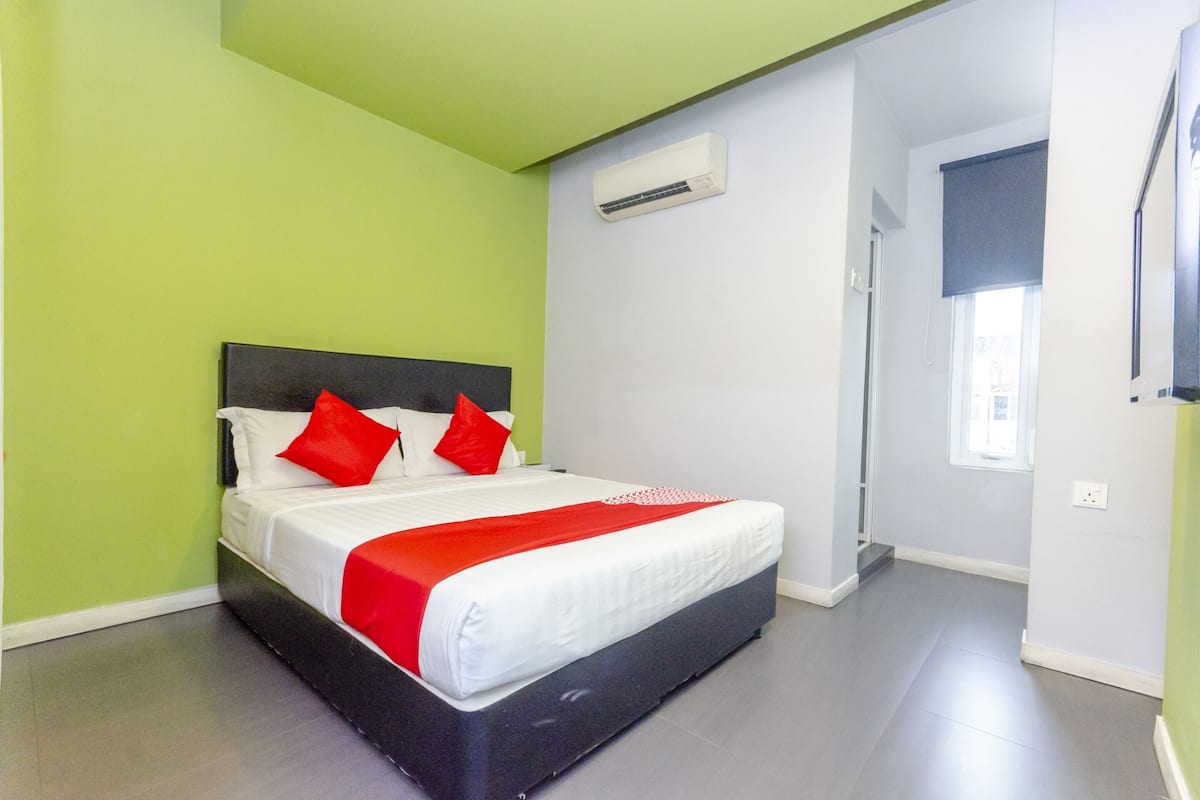 Une chambre d’hôtel avec un lit, une couvre-lit rouge et blanche et un sol gris.