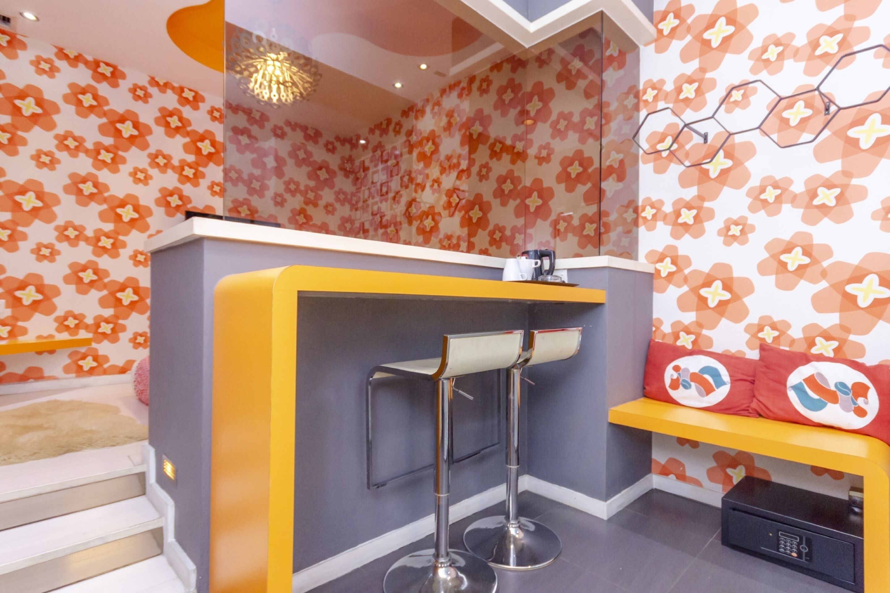 A modern bar area with a yellow counter, two bar stools, and a seating bench with a floral wall pattern.