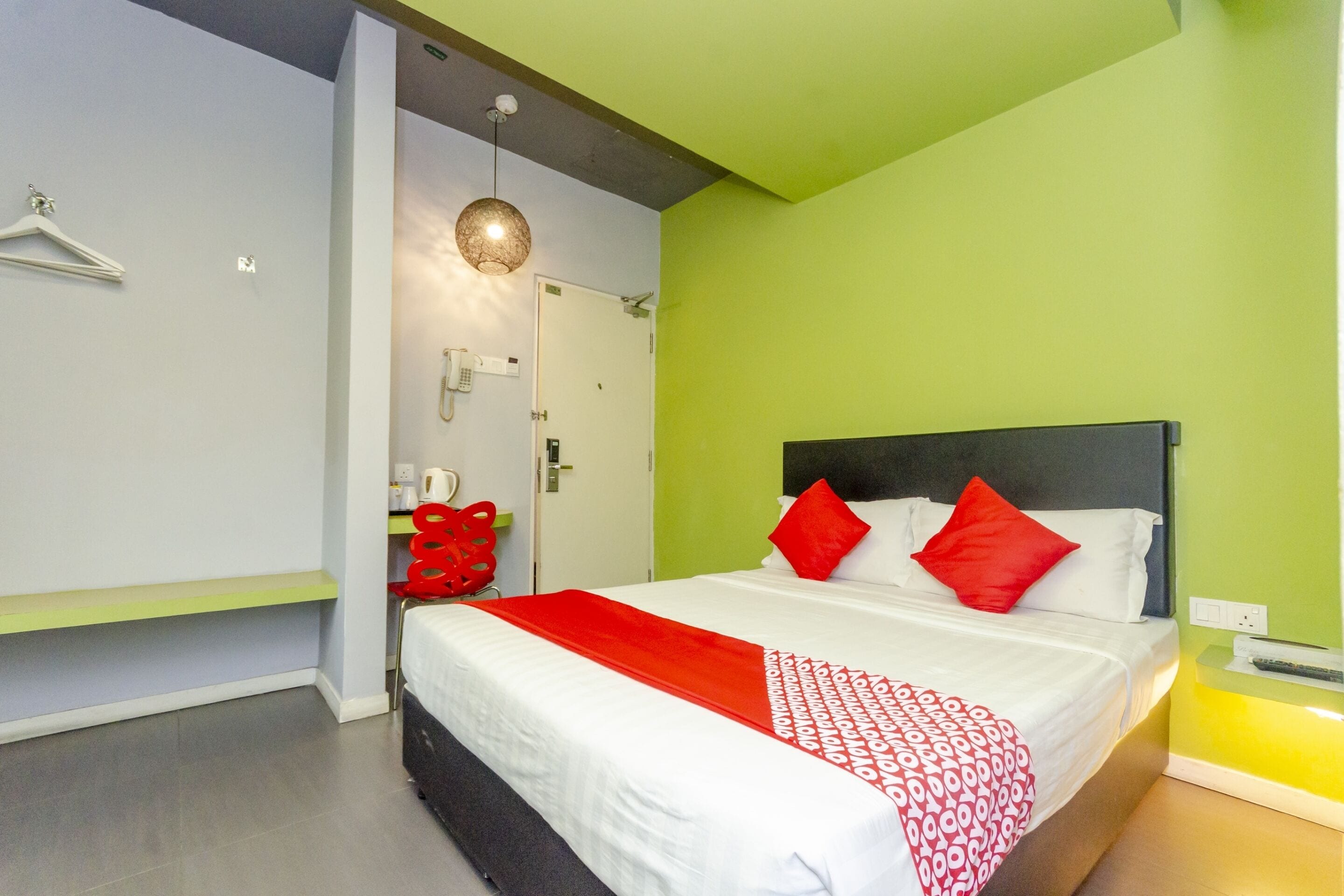 Una habitación de hotel moderna con una cama grande, ropa de cama roja y blanca, una pared de acento verde y un escritorio pequeño con una silla.