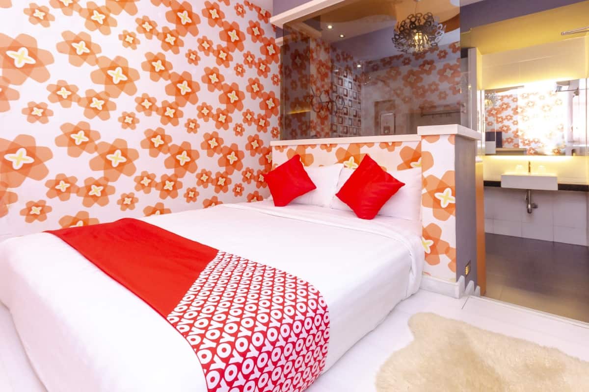 Une chambre moderne avec un grand lit, une literie à motifs rouges et blancs, une table de chevet blanche et une salle de bain avec un miroir et un lavabo.