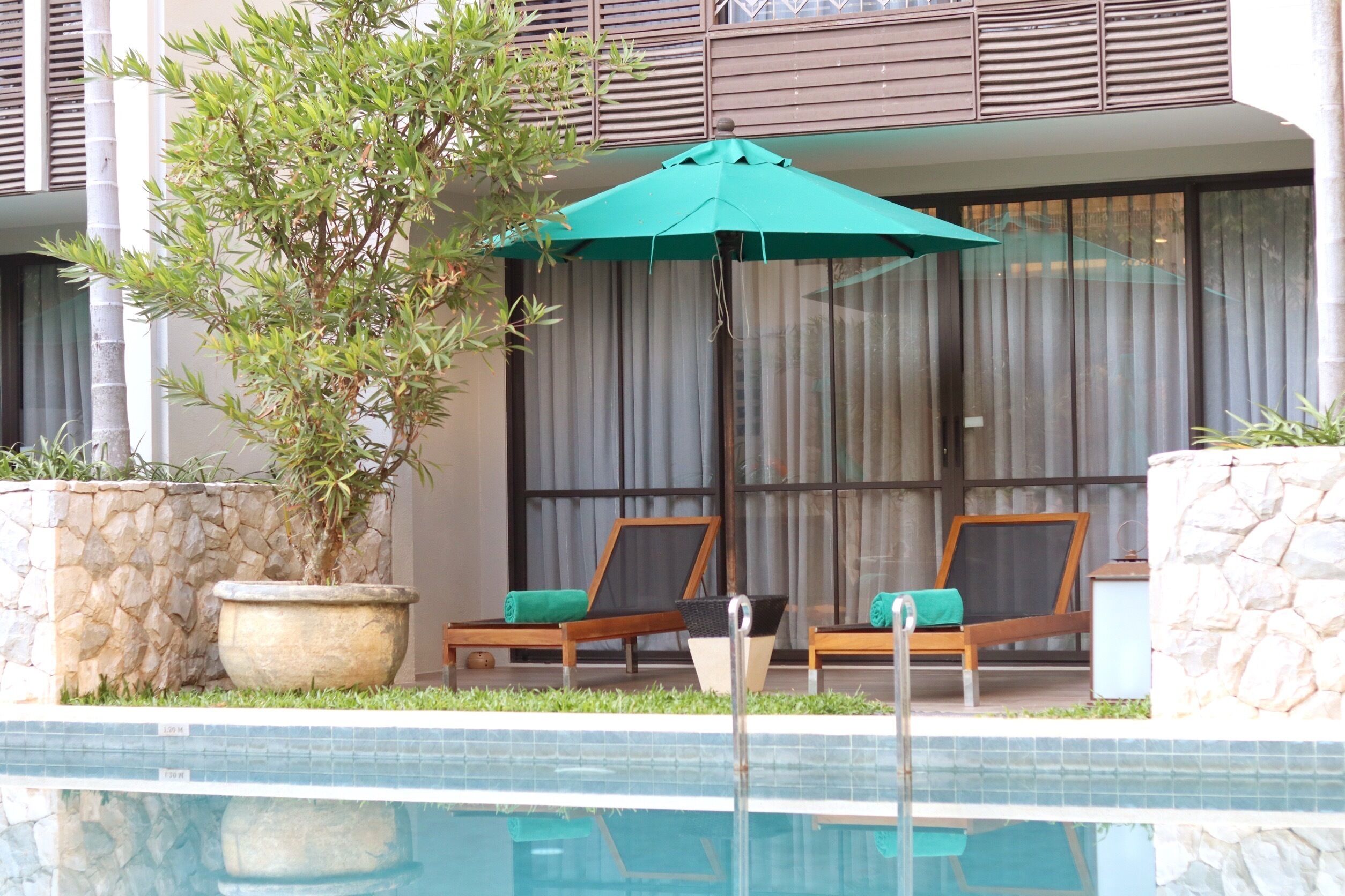 A poolside area with two lounge chairs, a large umbrella, and a potted plant.
