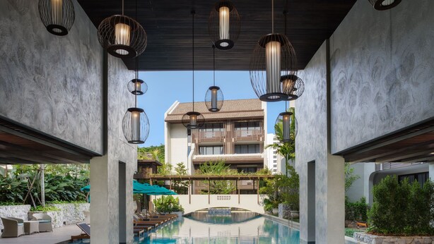 A modern indoor swimming pool with a circular design, surrounded by lounge areas and a multi-story building in the background. - Maladee Rendezvous Hotel Chiang Mai (Chiang Mai)