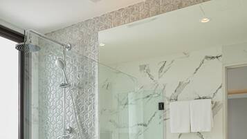 Un baño moderno con ducha de vidrio, inodoro blanco, pared con azulejos de mármol y un lavabo azul grande en el tocador.