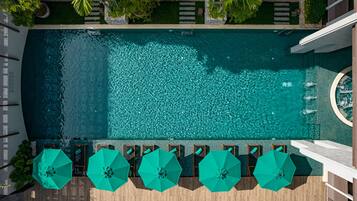 An aerial view of a rectangular swimming pool with clear blue water, surrounded by wooden deck seating and green umbrellas.