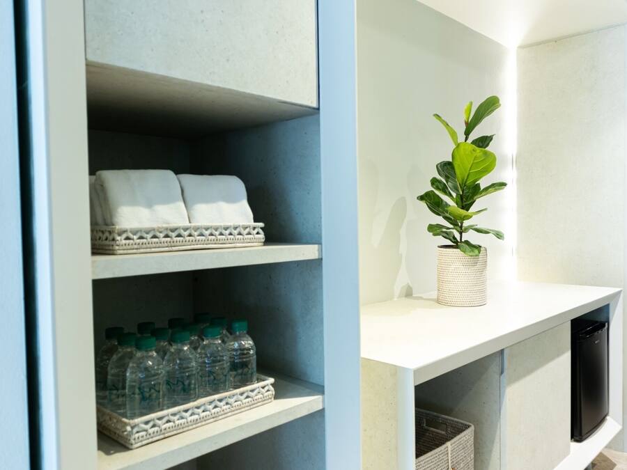 A modern bathroom with a white vanity, a plant, and neatly arranged towels and toiletries.