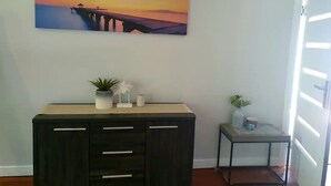 A room with a dark wooden cabinet, a small table with a plant, and a painting of a sunset over water on the wall.