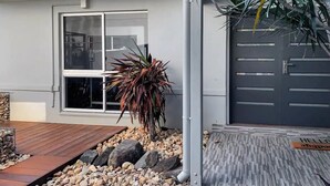 A modern house with a garage, a small garden with rocks and a plant, and a wooden deck.