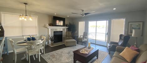 A living room with a fireplace, a dining area with a table and chairs, and a balcony with a chair.
