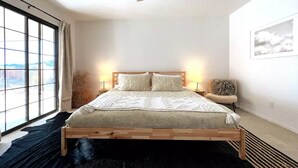 Una camera da letto con un letto grande, due lampade sui comodini, una ventola a soffitto, vista attraverso un'ampia finestra e un quadro appeso al muro.