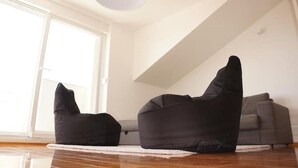 Ein Zimmer mit großem Fenster, einem schwarzen Sitzsack, einem grauen Sofa und Holzboden.