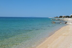 A beach with clear water, a sandy shore, and a pier extending into the sea. - Ferienwohnung "calimero" - mit Meerblick (Novalja)