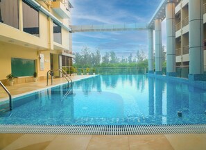 Una piscina interior con agua azul cristalina, rodeada por un solado de baldosas y plantas en macetas.