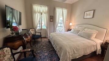 Una habitación de hotel con una cama, un escritorio con silla, un televisor y un ventanal con cortinas.