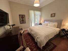 Habitación de hotel con una cama grande, un escritorio con una silla, televisión, ventana con cortinas y un cuadro en la pared.