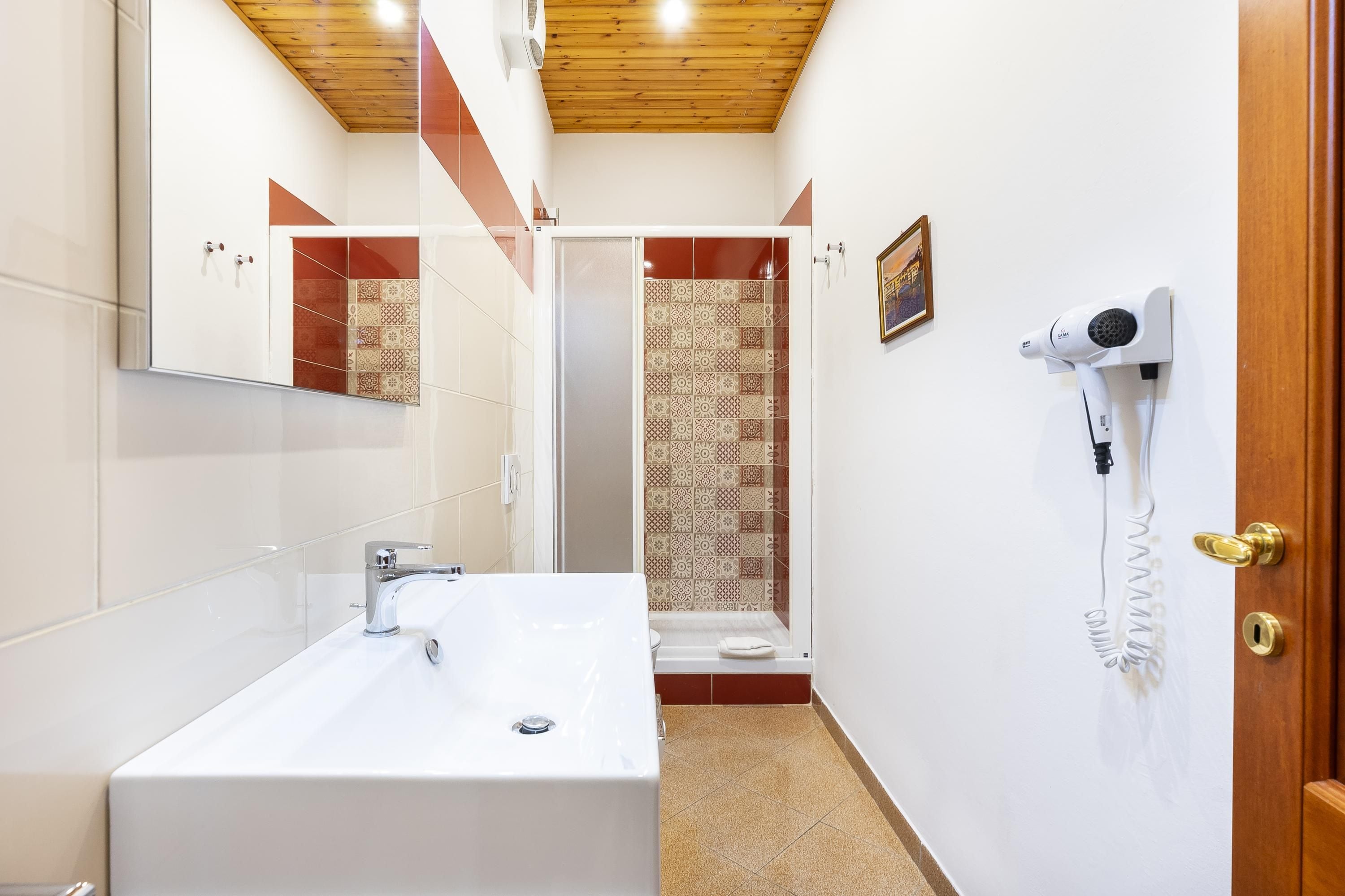 Een moderne badkamer met een groot wastafel, een douche met patroon betegelde wanden, en een haardroger bevestigd aan de muur.