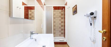 Een moderne badkamer met een groot wastafel, een douche met patroon betegelde wanden, en een haardroger bevestigd aan de muur.