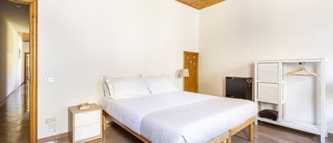Un dormitorio con un cabecero de madera, una mesita de noche blanca, un armario y una puerta que da a otra habitación.