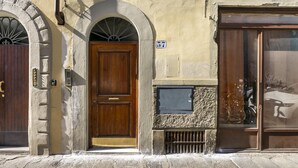 A building with a wooden door, a stone wall, and a window with a bicycle inside. - Ruote for Three in Firenze (Florence)