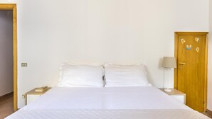 A neatly made bed with white linens, a wooden nightstand with a lamp, and a wooden door with angel decorations. - Ruote for Three in Firenze (Florence)