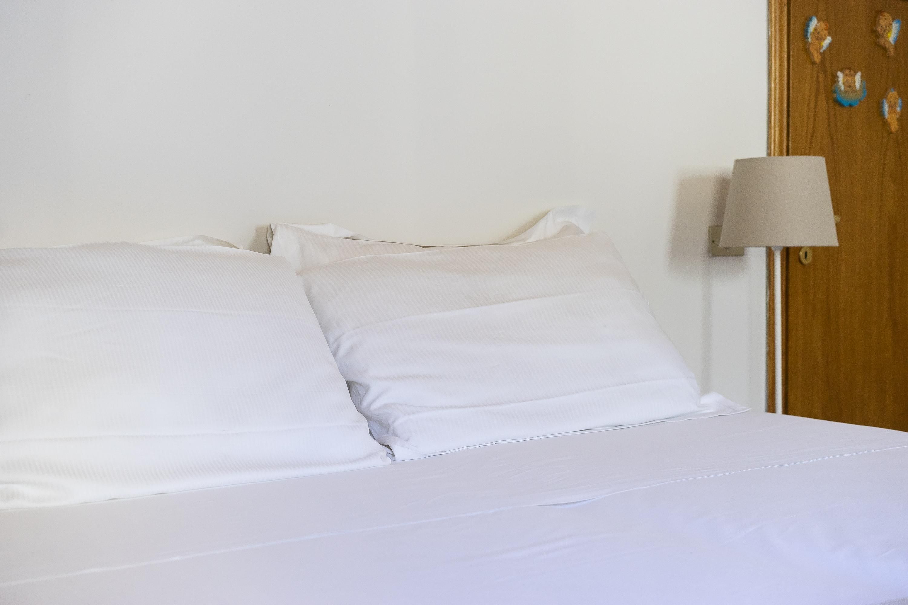 A bed with white linens and a lamp beside it.