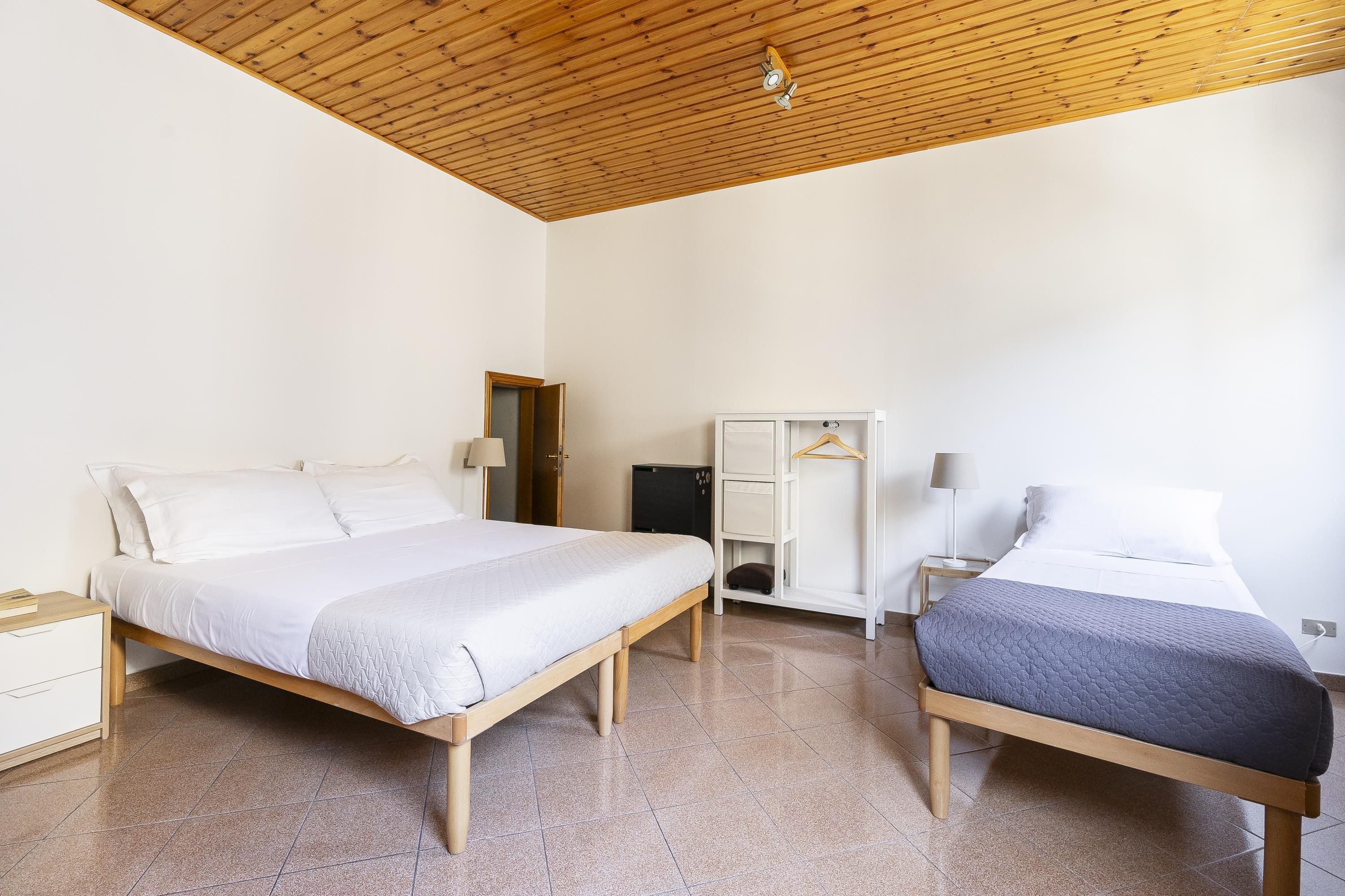 Une chambre avec deux lits, un plancher en bois, une armoire et un bureau avec une lampe.