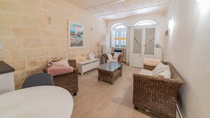 A cozy room with stone walls, wicker furniture, and a glass coffee table. - Central Valletta Townhouse (Valletta)