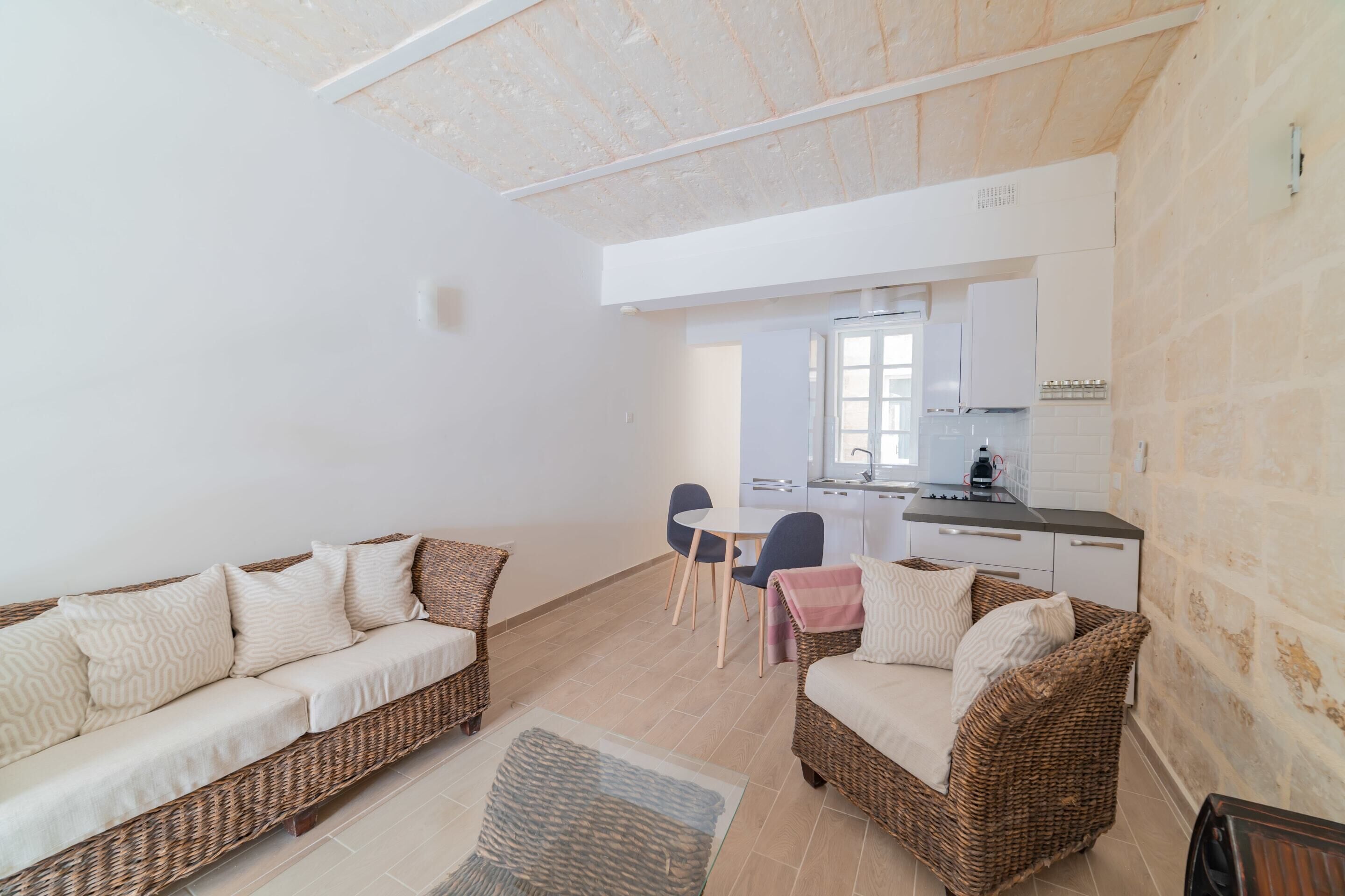 Un salon moderne avec un canapé, des fauteuils et une table à manger. On aperçoit une cuisine au fond.