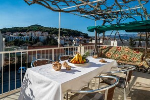 A terrace with a table set for dining, overlooking a hillside town. - Apartment Bozica (Dubrovnik)