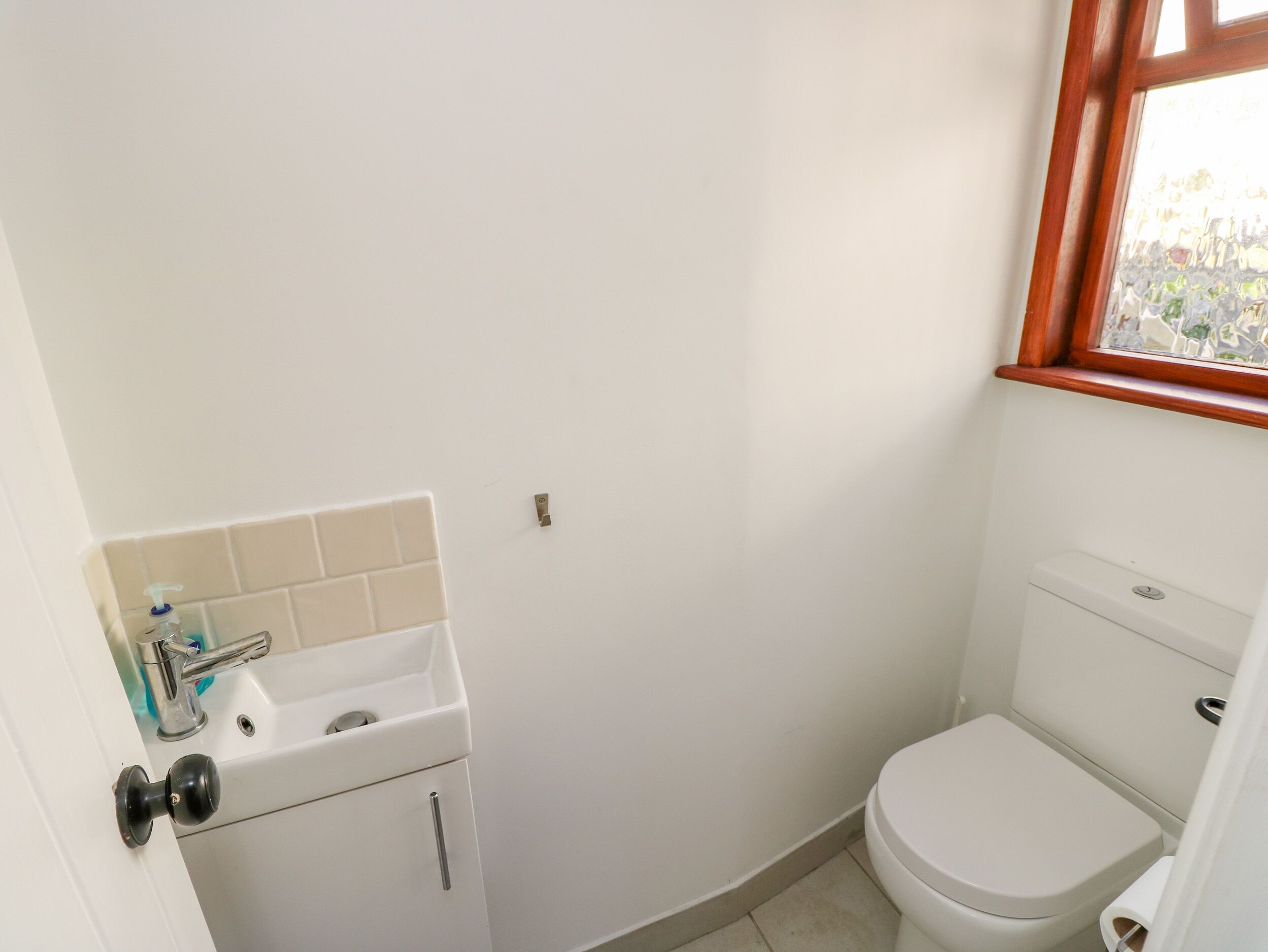 A small, clean bathroom with a white sink, toilet, and a window with a wooden frame.