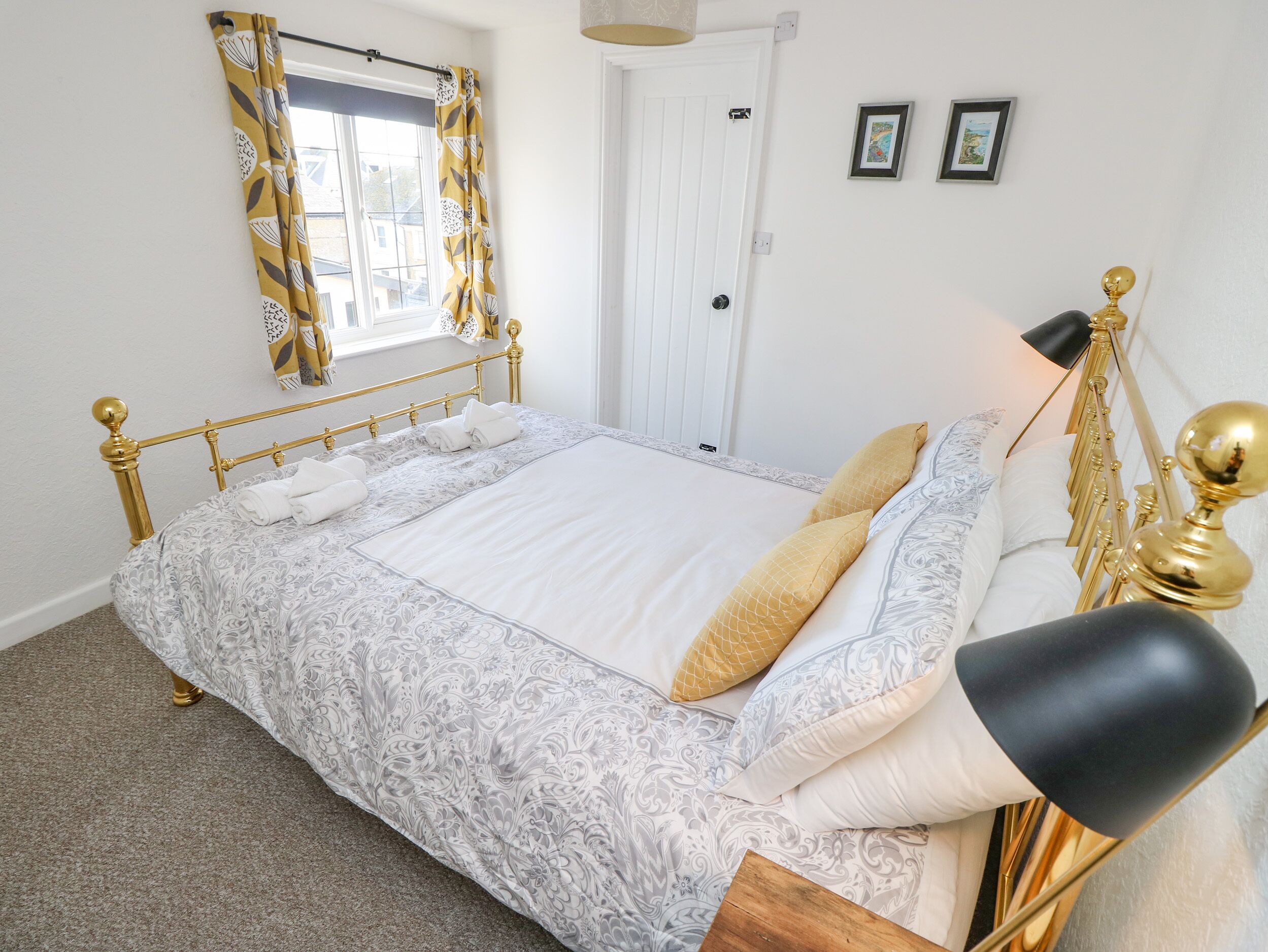 A neatly made bed with a patterned bedspread and pillows, a gold-framed headboard, and a black lamp beside it.