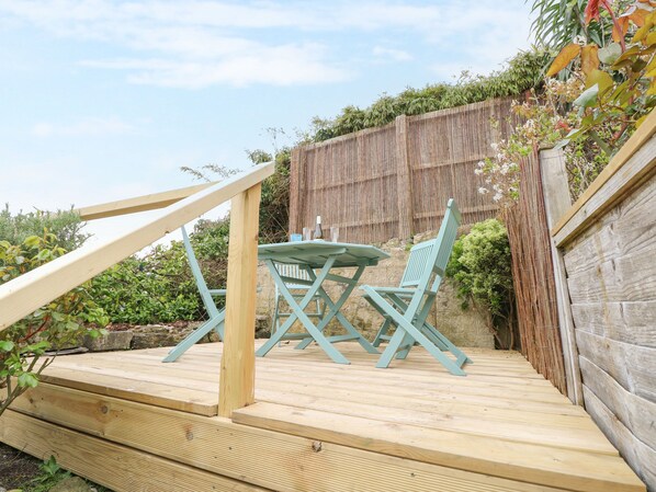 A wooden deck with a table and chairs, a wooden railing, and a bamboo fence in the background.