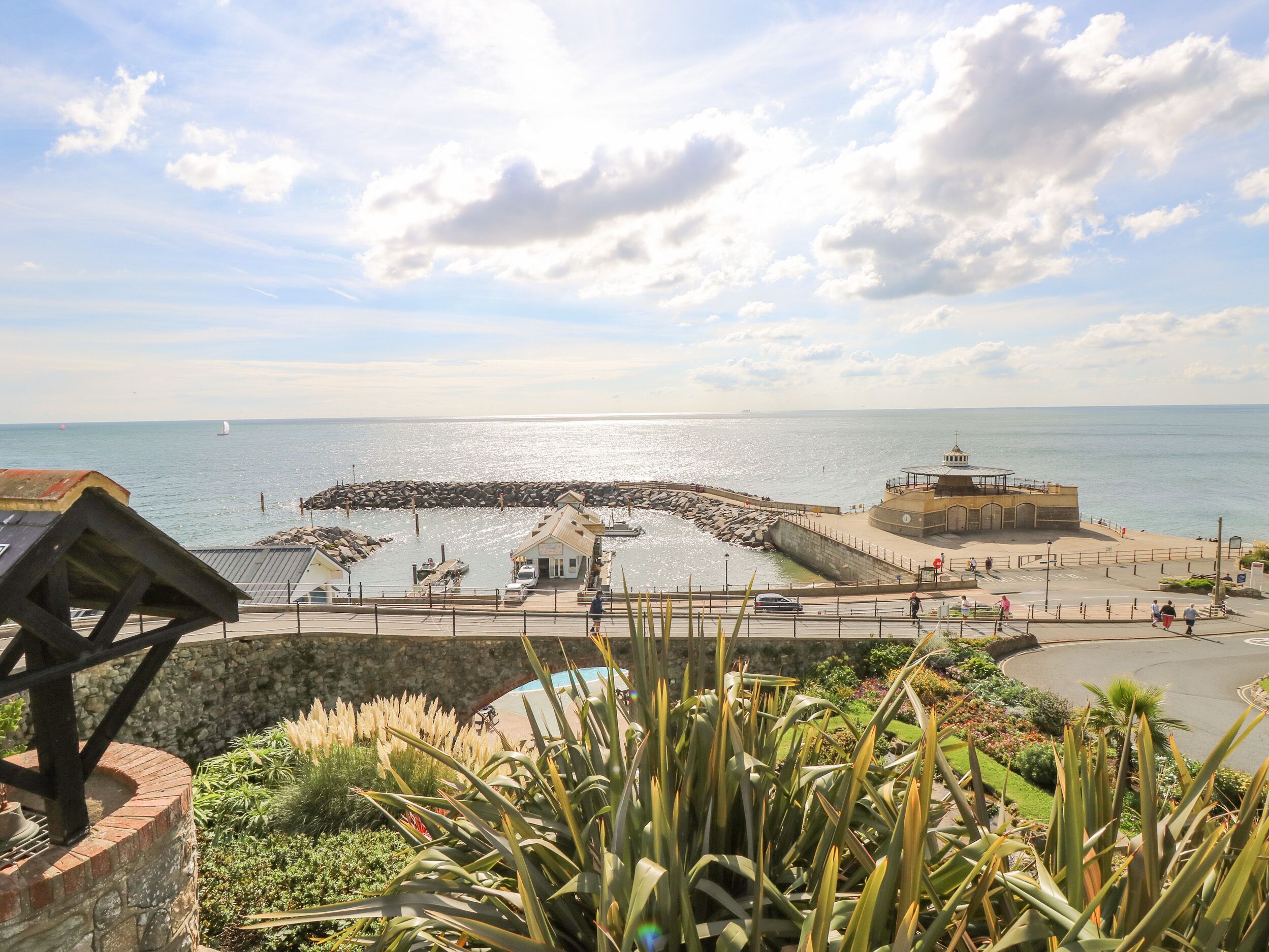 A coastal promenade with a stone pier, a small building, and a lighthouse-like structure.