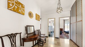 Un pasillo espacioso con piso de madera, un comedor con mesa y sillas, y una habitación con cama y un ventanal grande.