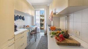 Cocina compacta con armarios blancos, una mesa de comedor con sillas y una variedad de frutas y verduras frescas en la encimera.