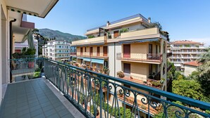 Un edificio residencial de varios pisos con balcones, una terraza con tejas y una montaña al fondo.