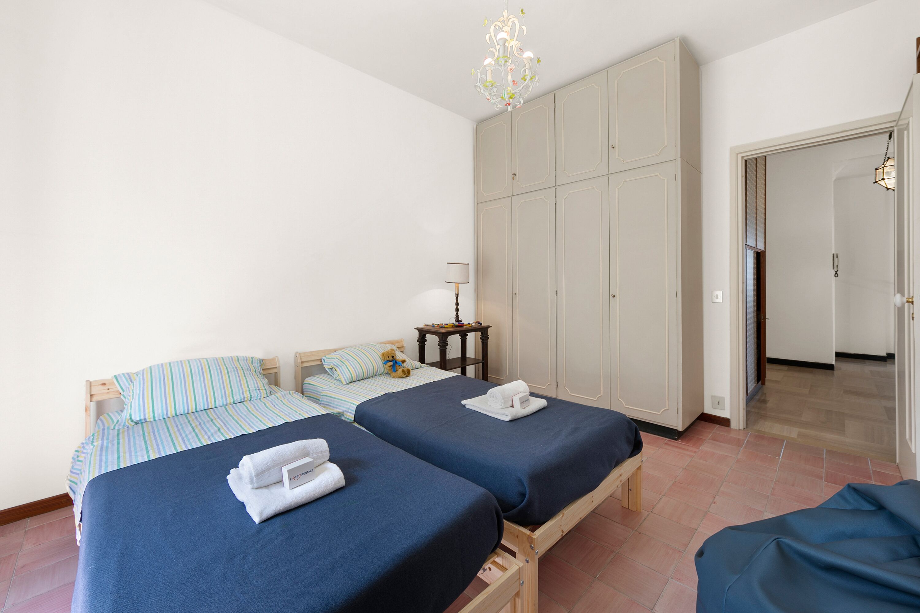 A room with two beds, a wardrobe, a nightstand, and a hanging light fixture.