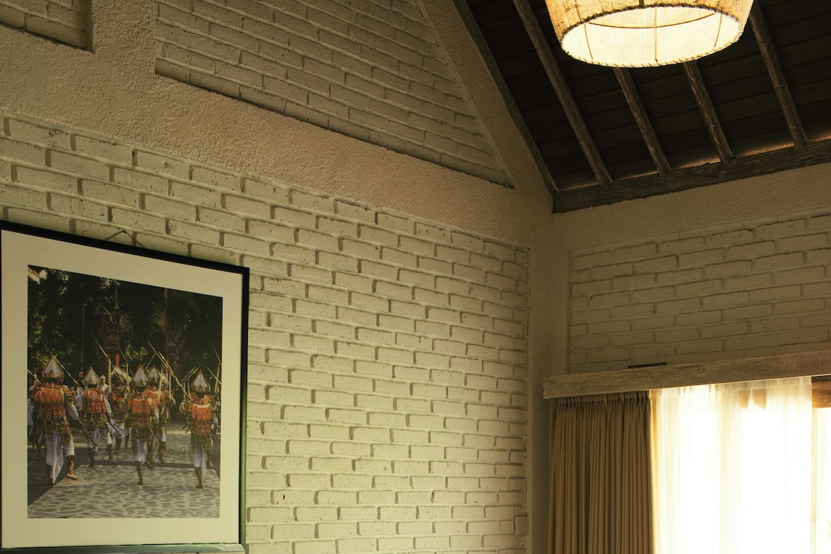 A hotel room with a brick wall, a large bed, a framed picture, and a window with curtains.
