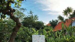 A wooden deck with two wicker lounge chairs, a swimming pool, and lush greenery. - Tamuku Padang Padang, CARI Surf Camp (Pecatu)