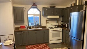 A kitchen with dark cabinets, a white stove, a stainless steel refrigerator, and a window with a view of trees. - Sunset views in the foothills (Rough and Ready)