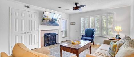 A living room with a fireplace, a television, and a ceiling fan.