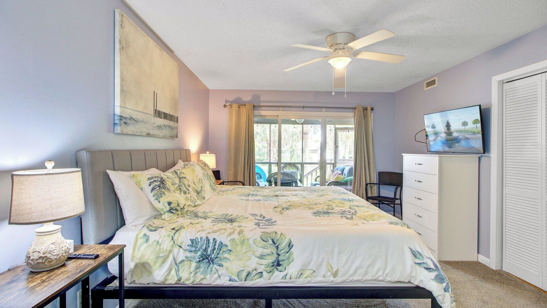 A bedroom with a bed, a ceiling fan, a TV, and a window with curtains.